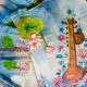 Saraswati theme hand painted artificial muslin saree from KhatiBaazaar featuring a traditional veena and pink lotus design on a white and blue gradient backdrop